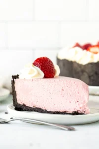 Slice of no bake strawberry cheesecake topped with whipped cream and a strawberry