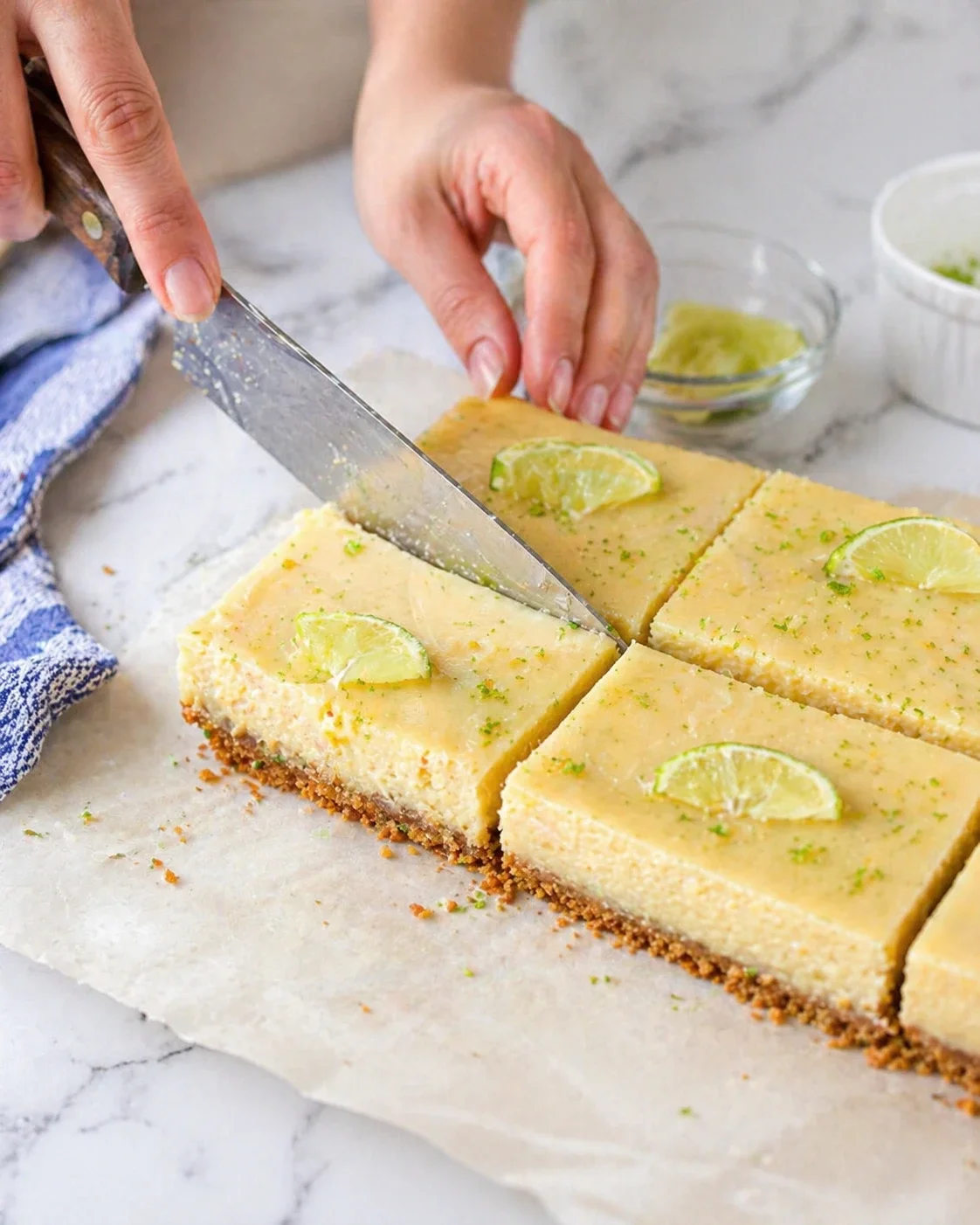close-up of creamy lime cheesecake bars being sliced on parchment with lime wedges garnish