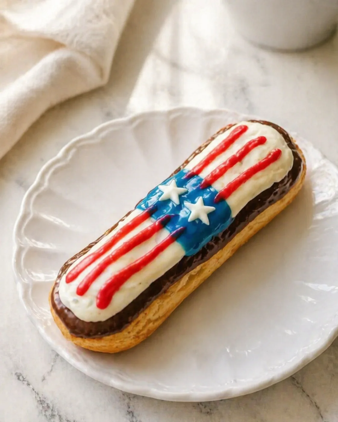 elongated éclair topped with white icing, red stripes, and a blue field with white stars on a white plate.