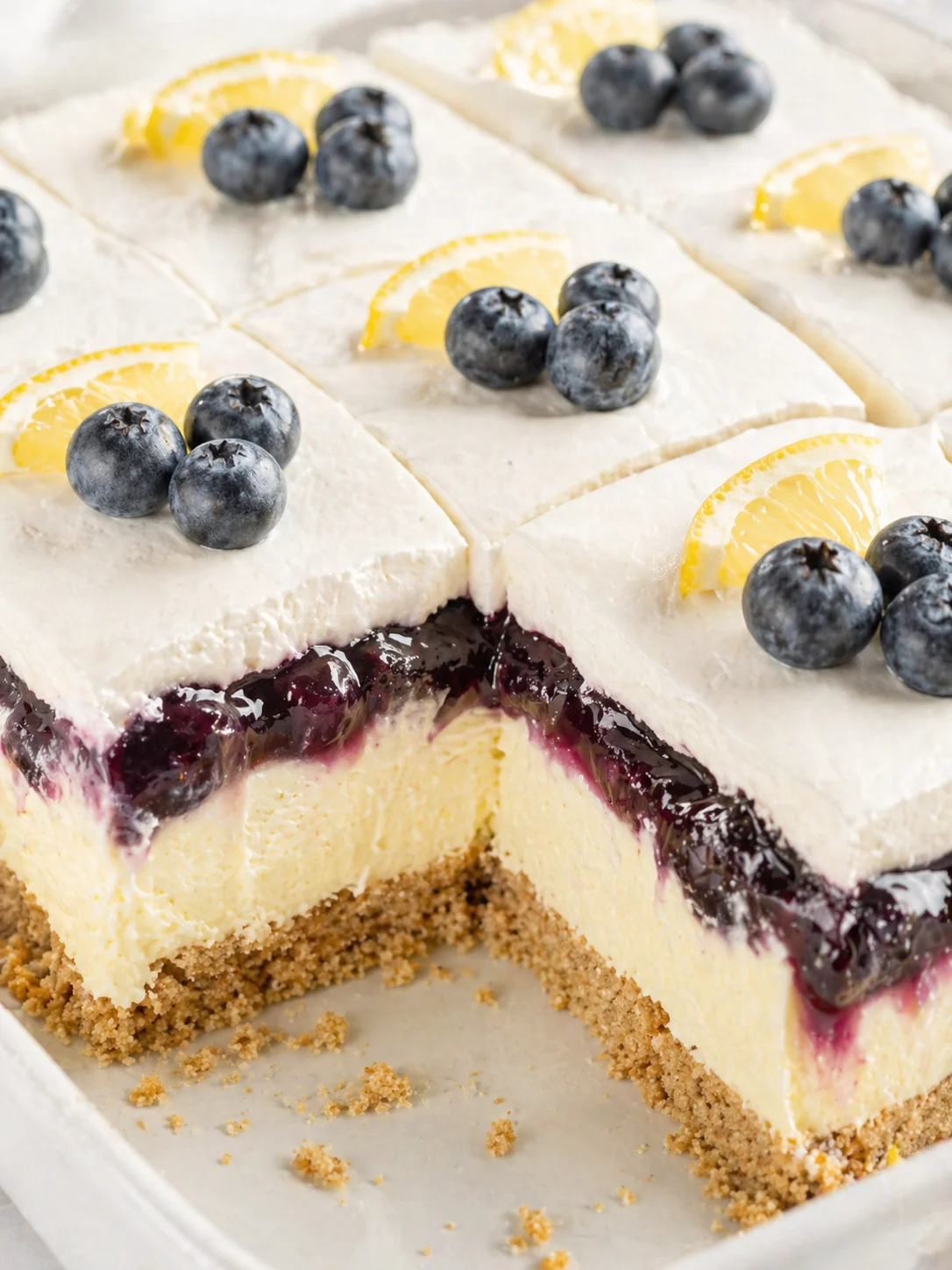 Creamy lemon cheesecake with blueberry topping and crumb crust, garnished with lemon wedges and blueberries.