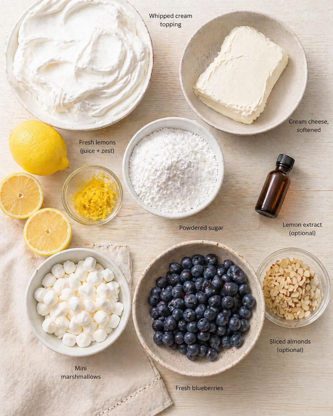 Flat lay of whipped cream topping, cream cheese, powdered sugar, lemons, blueberries, marshmallows, sliced almonds, lemon extract bottle