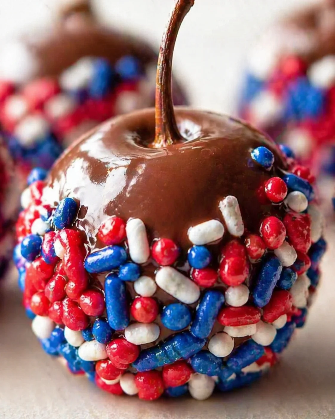 Close-up of a chocolate-dipped apple encrusted with red, white, and blue candy sprinkles.