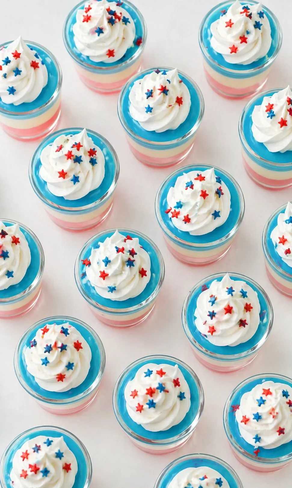 Glass dessert cups with pink, white, and blue layers topped with whipped cream and red-blue star sprinkles.
