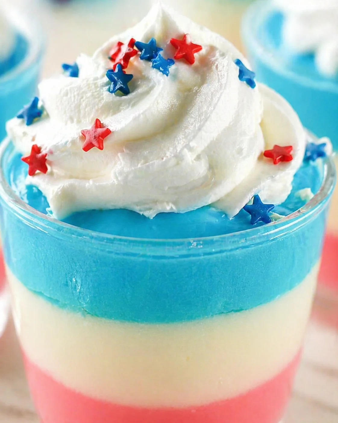 Close-up of a patriotic layered dessert drink topped with whipped cream and star sprinkles.