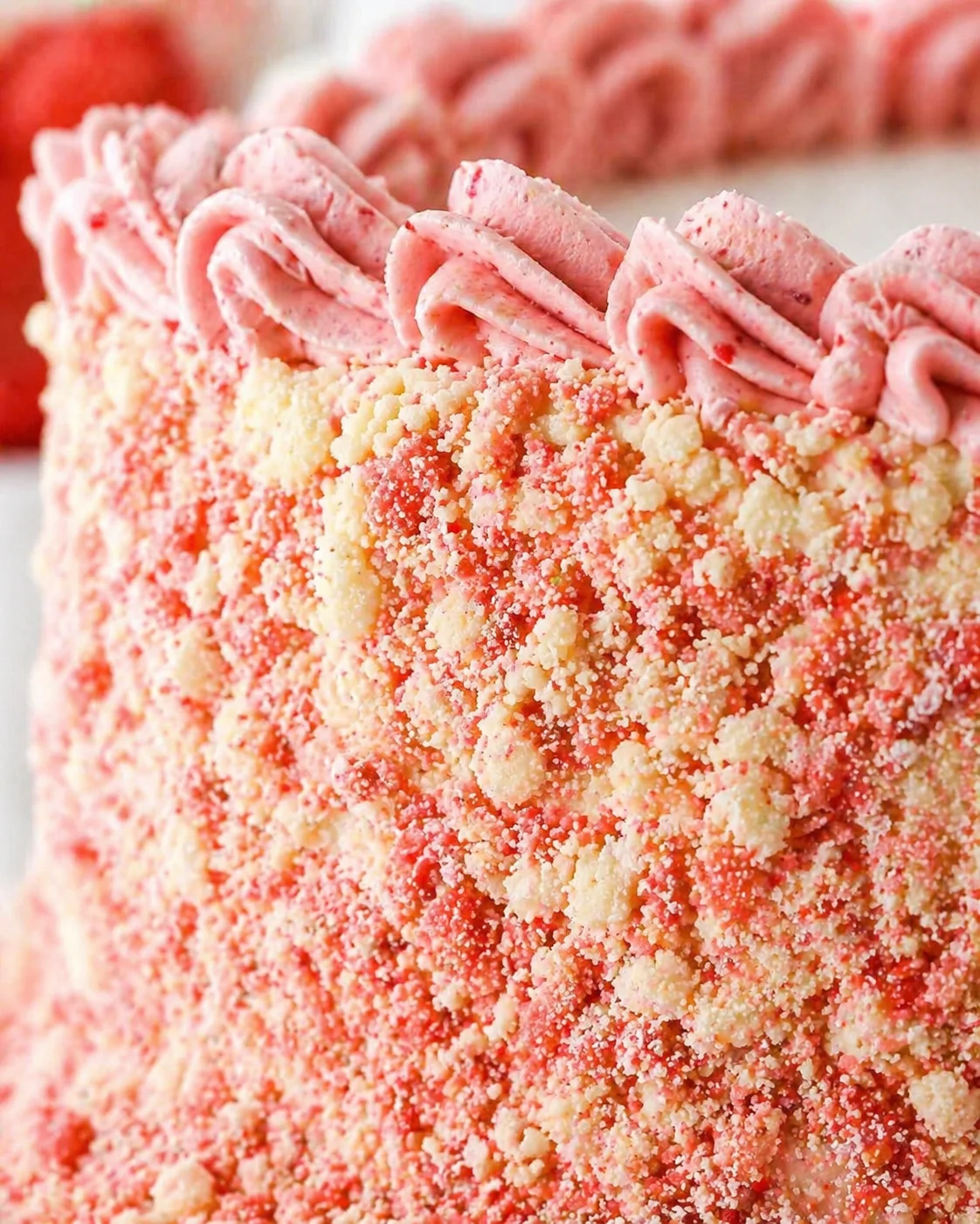 Close-up view of a cake with pink rose piping on the top edge and crumbly pink-cream coating on the side.