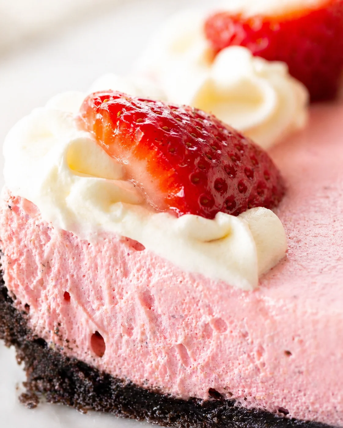 Close-up of a pink strawberry cheesecake slice topped with whipped cream and a fresh strawberry half
