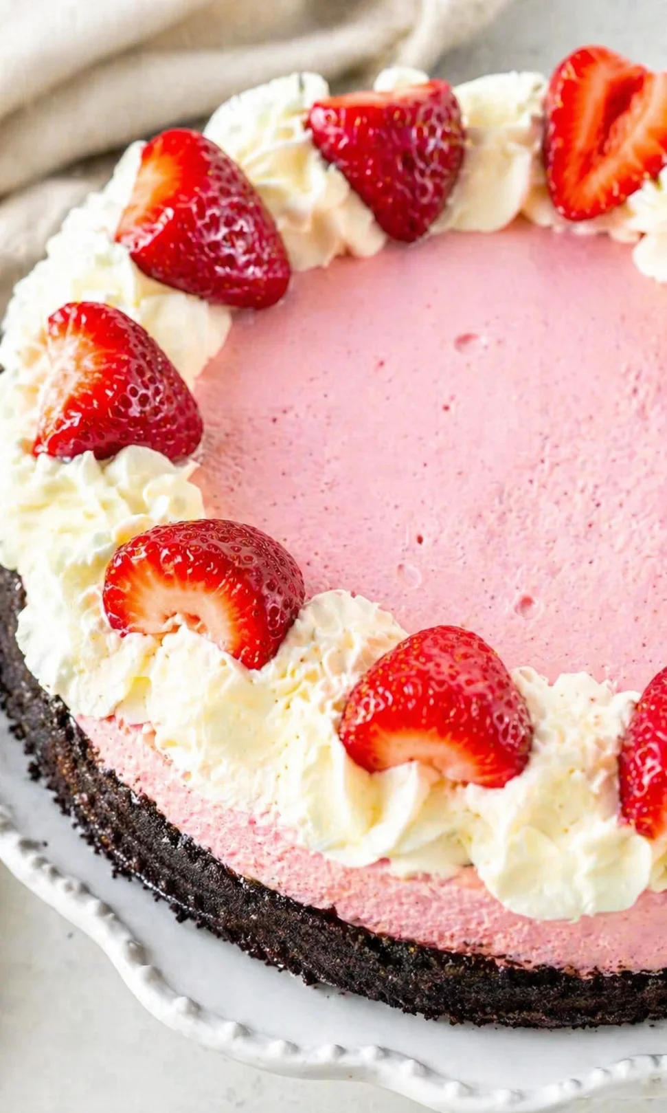 Close-up of pink strawberry cheesecake with whipped cream and fresh strawberries on a white plate