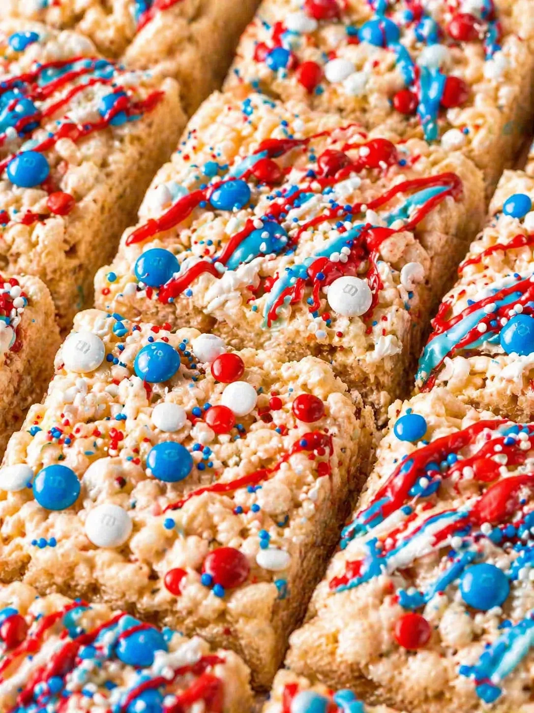 Close up of rectangular cereal bars decorated with red and blue drizzle and colorful candies.