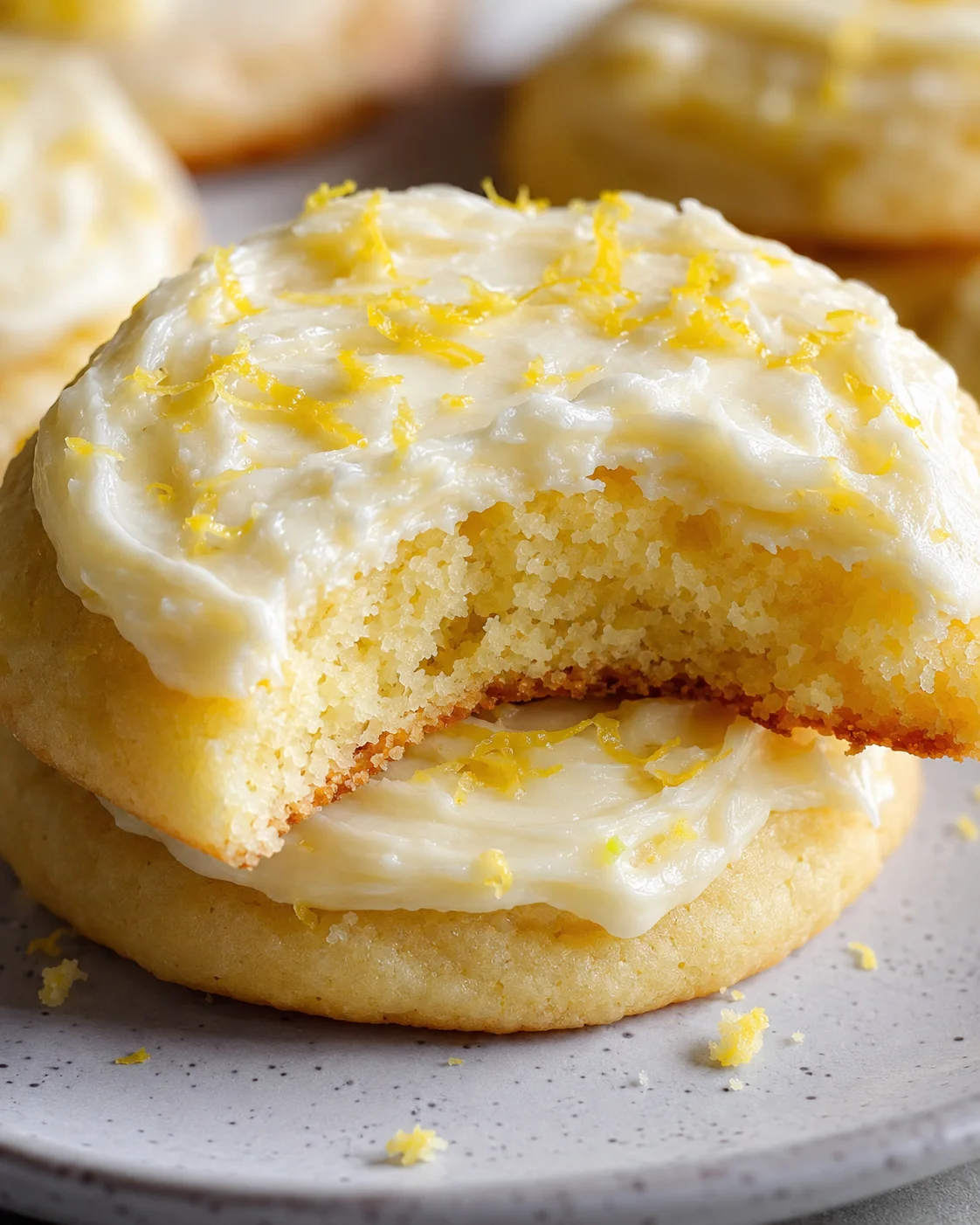 Close-up of soft, lemon-flavored frosted cookies with yellow zest on top.