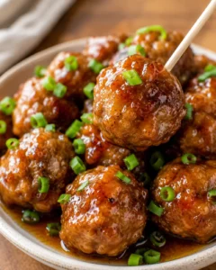 Close-up of juicy meatballs coated in apple glaze garnished with green onions.