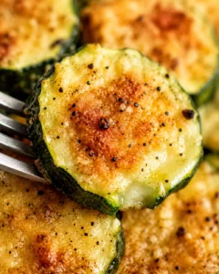 Close-up of crispy baked zucchini slices with cheese and seasoning.