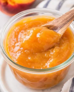 Homemade vanilla honey peach butter in a glass jar with a wooden spoon
