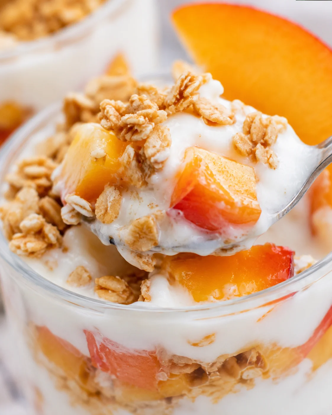 Close-up of a layered peach parfait with granola and creamy yogurt.