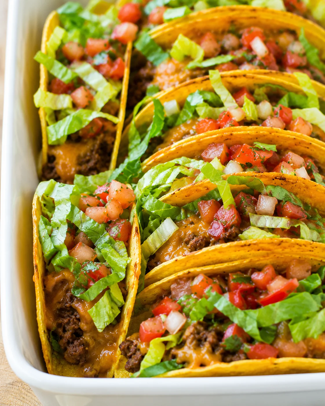 Close-up of baked beef tacos with lettuce and salsa in a baking dish
