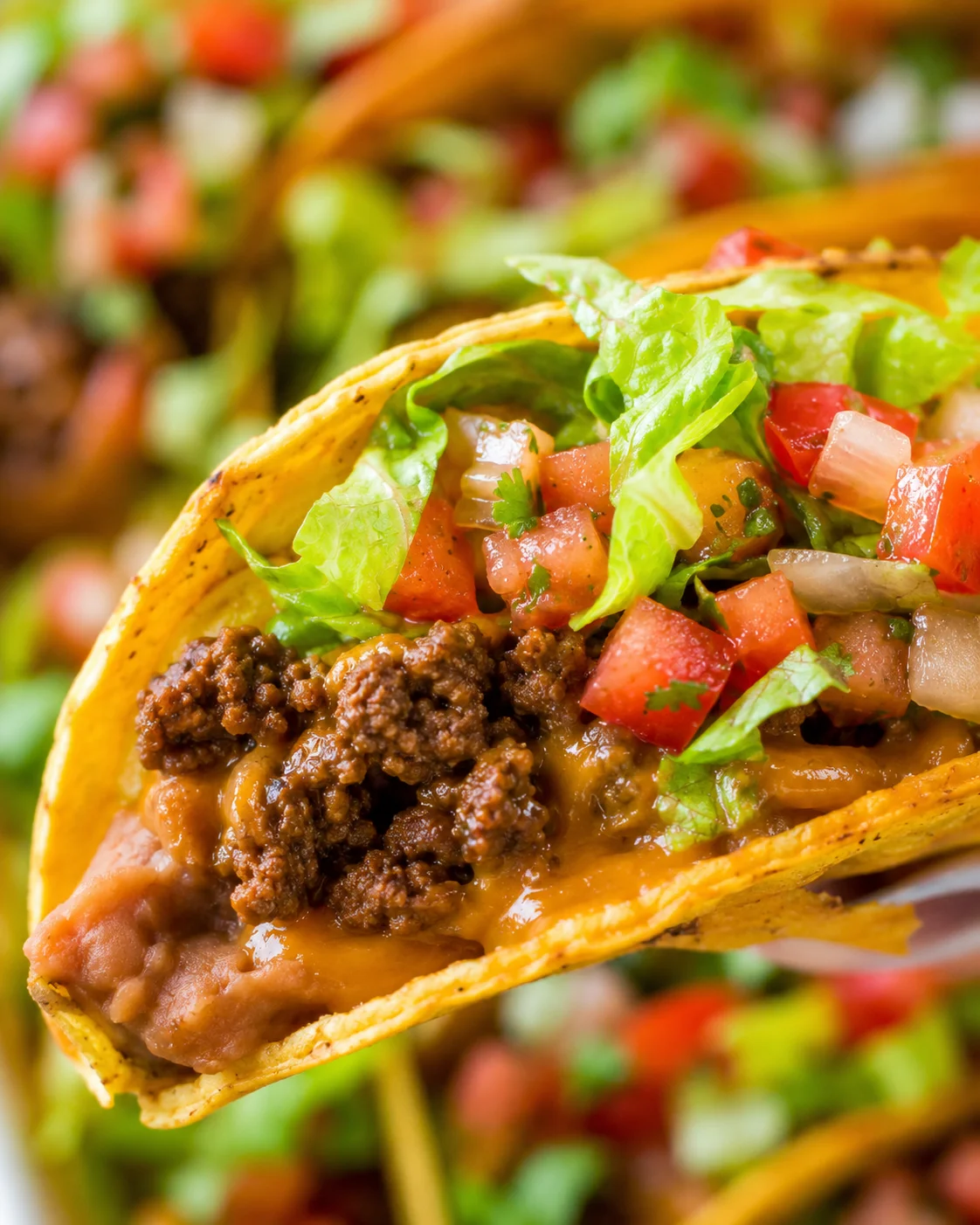 Close-up of baked beef tacos topped with lettuce, cheese, and salsa