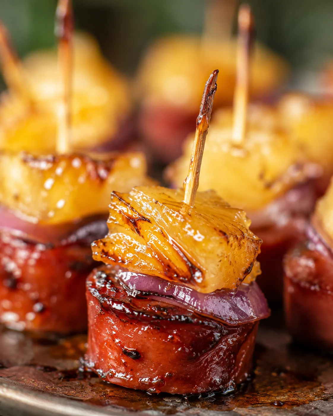 Close-up of caramelized pineapple sausage bites with glaze and red onion.