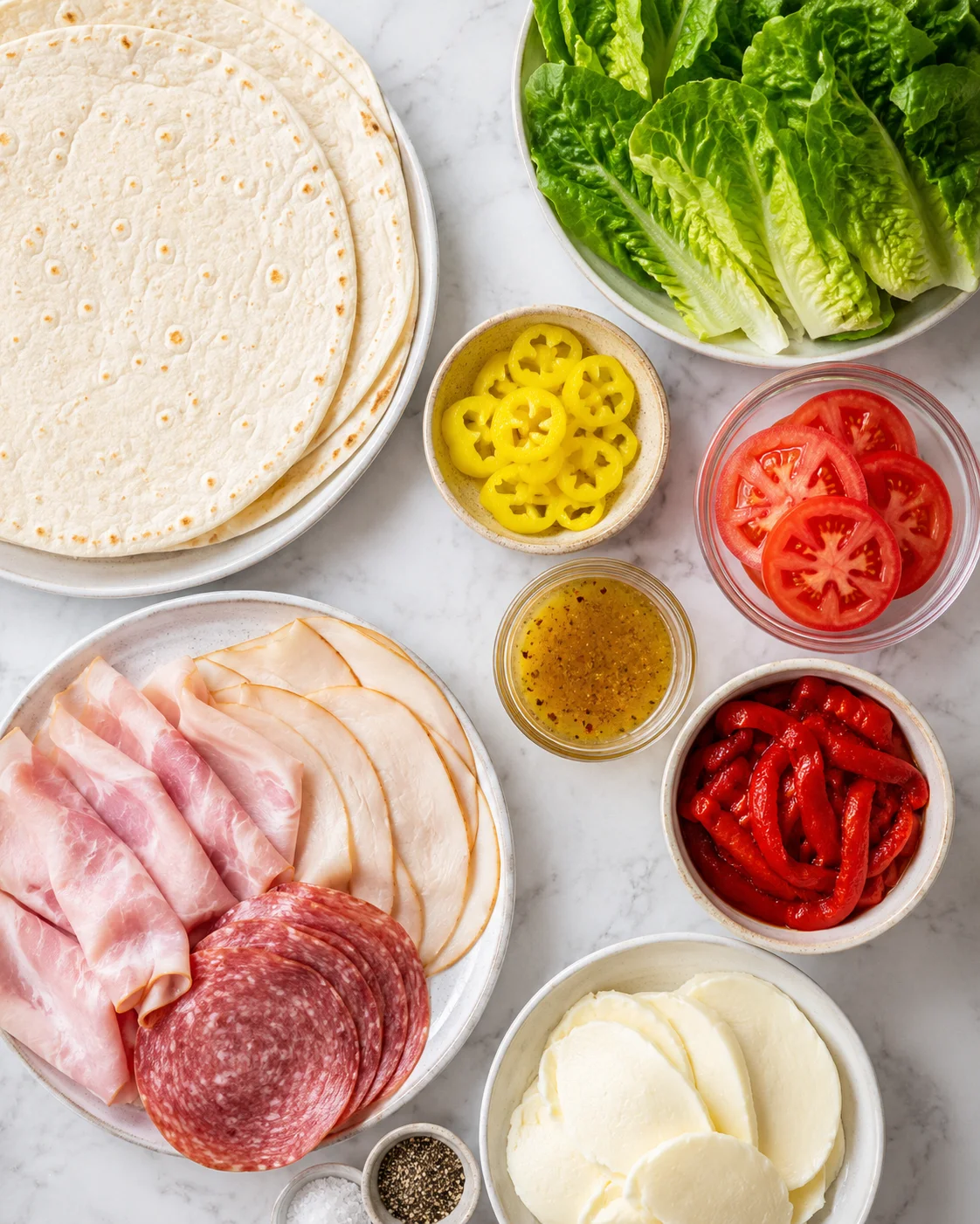 Assorted deli meats, cheeses, and vegetables ready for roll-ups on a marble surface.