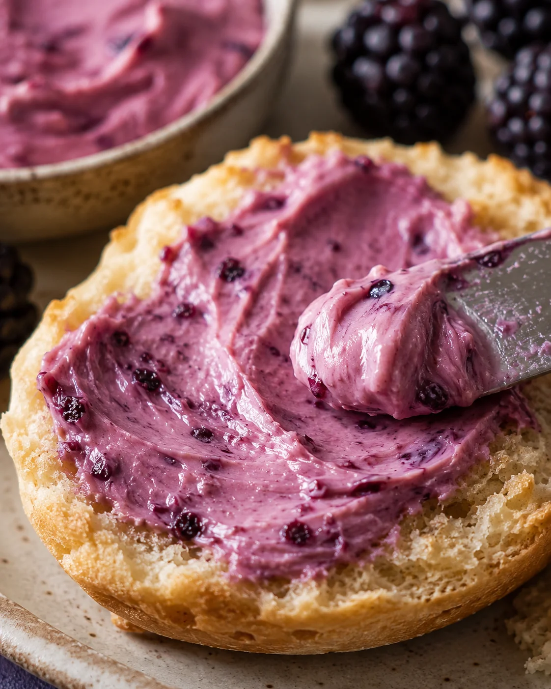 Creamy blackberry compound butter spread on bread with berries in background