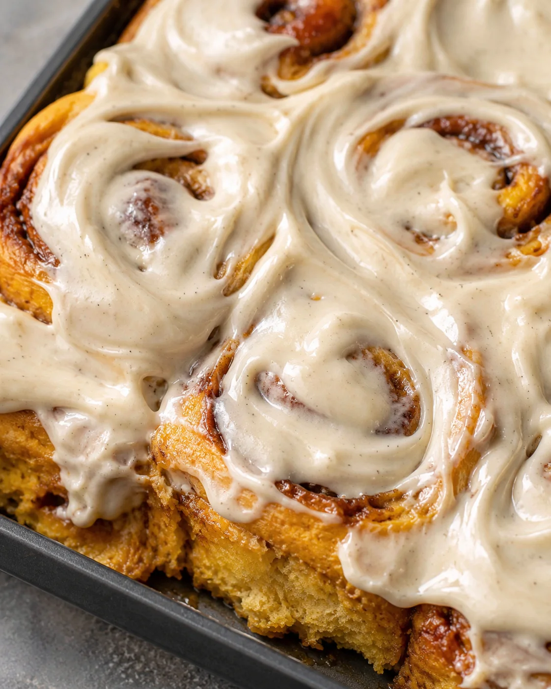Close-up of soft pumpkin cinnamon rolls topped with vanilla bean maple frosting