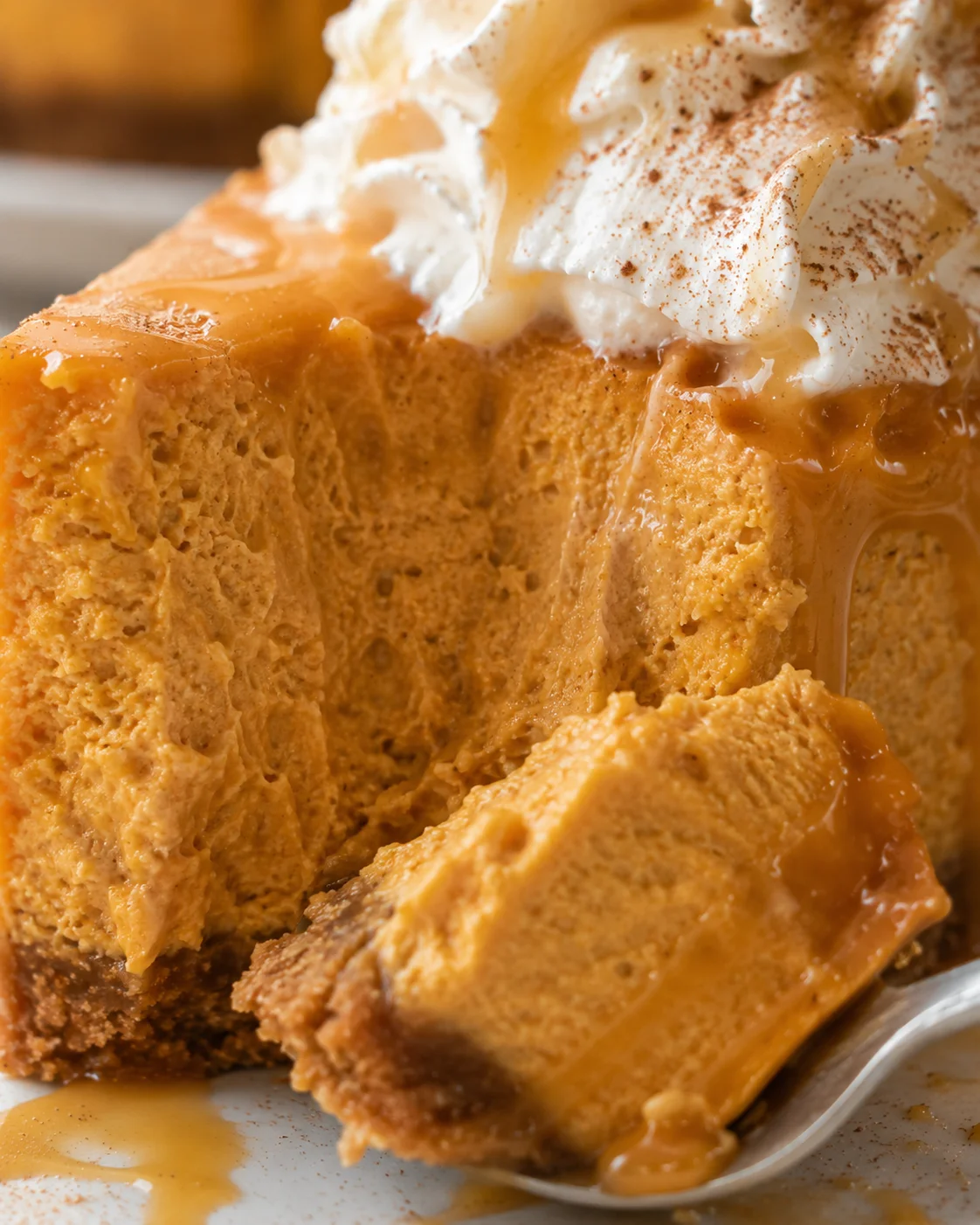 Close-up of a sliced pumpkin cheesecake with caramel sauce and whipped topping.