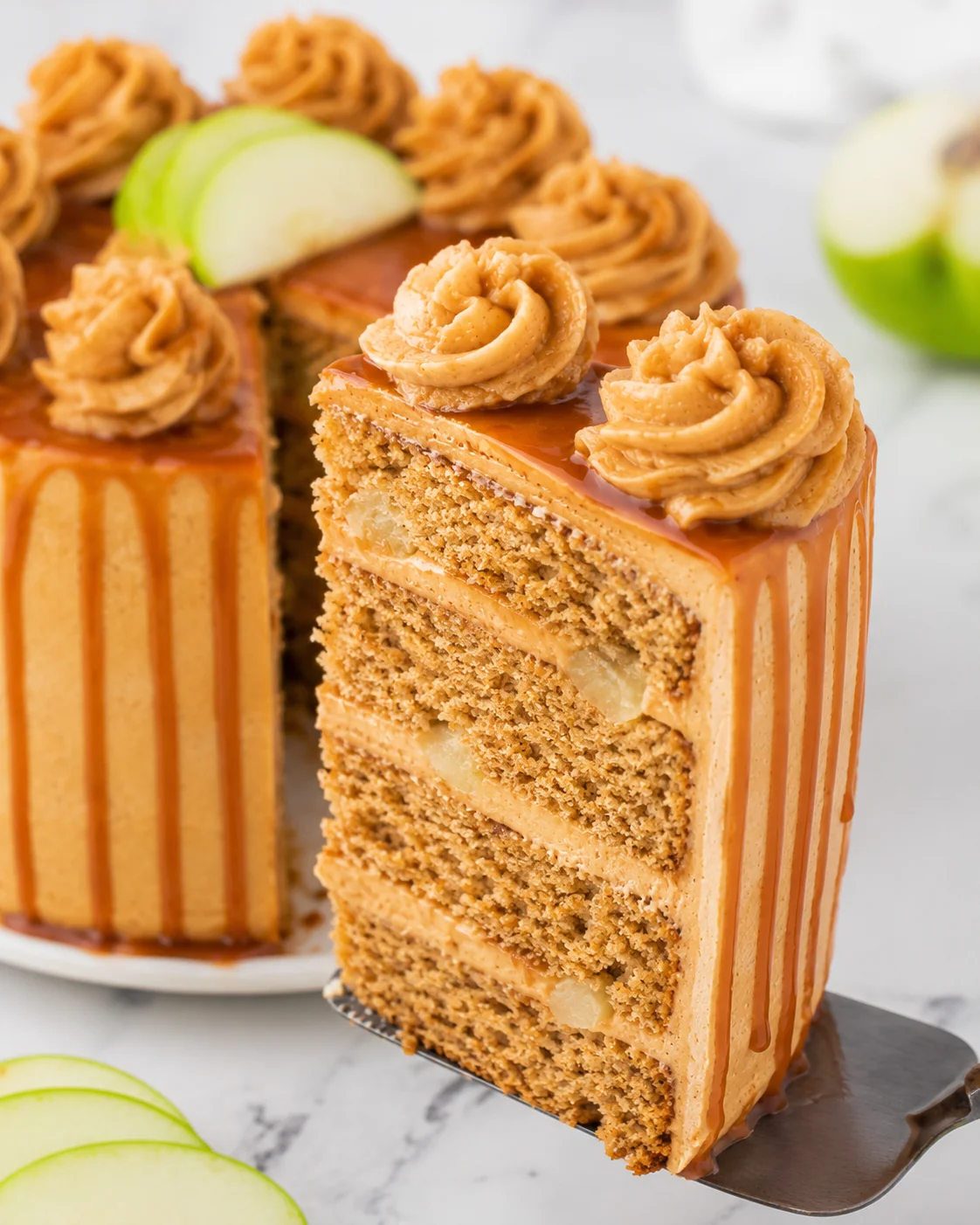 Close-up of a layered caramel apple spice cake with caramel drizzle and whipped frosting.