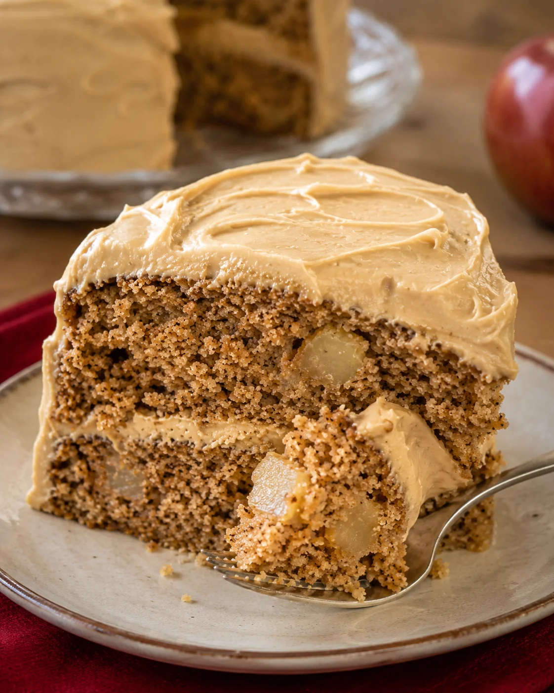 Slice of moist apple spice cake topped with caramel frosting and apple chunks