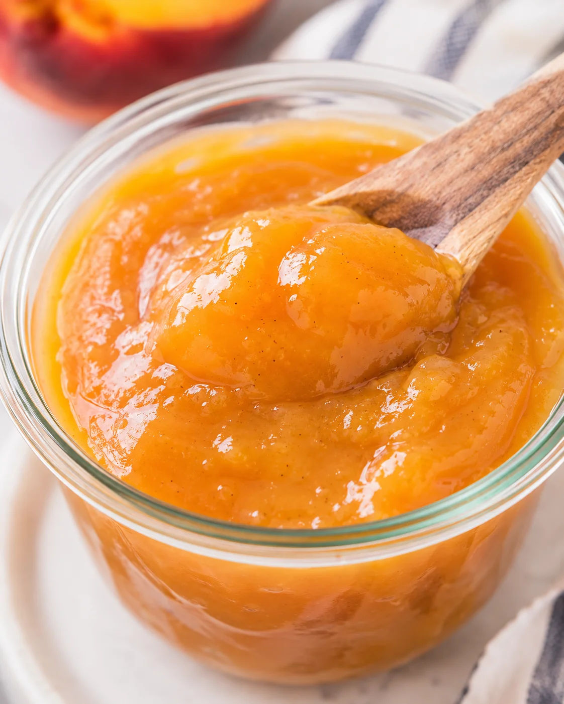 Homemade vanilla honey peach butter in a glass jar with a wooden spoon