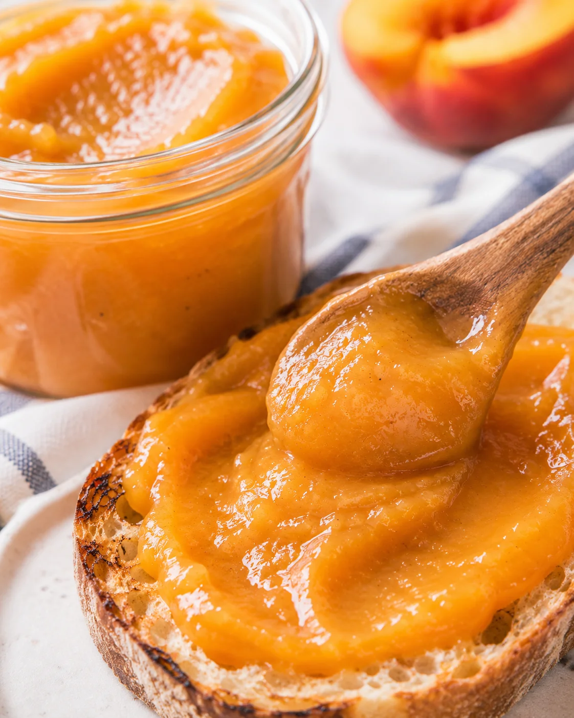 Close-up of homemade peach butter spread on toasted bread with a jar nearby.