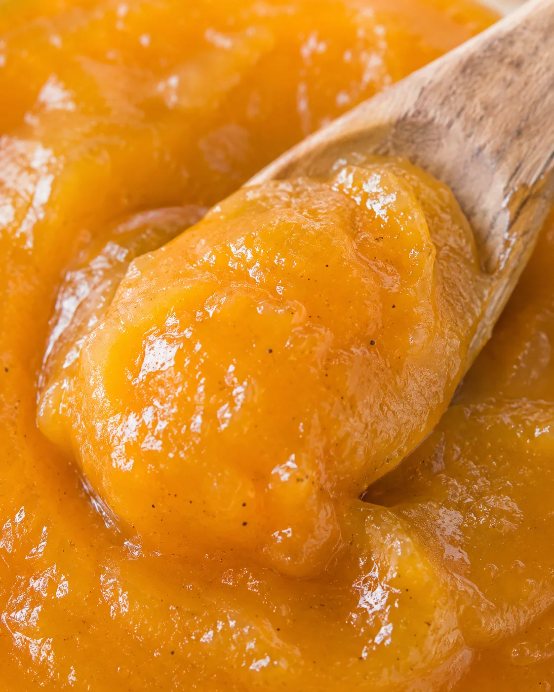 Close-up of golden peach butter with a wooden spoon, creamy and spreadable.