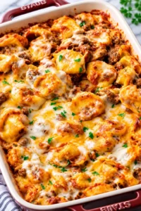 Cheesy baked tortellini with tomato meat sauce in a red Staub dish, sprinkled with parsley.