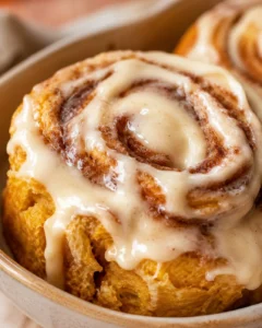 Delicious pumpkin cinnamon rolls with brown butter frosting on a baking dish.