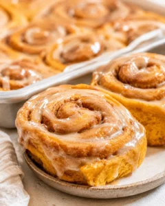 Delicious pumpkin cinnamon rolls topped with coffee maple frosting on a plate