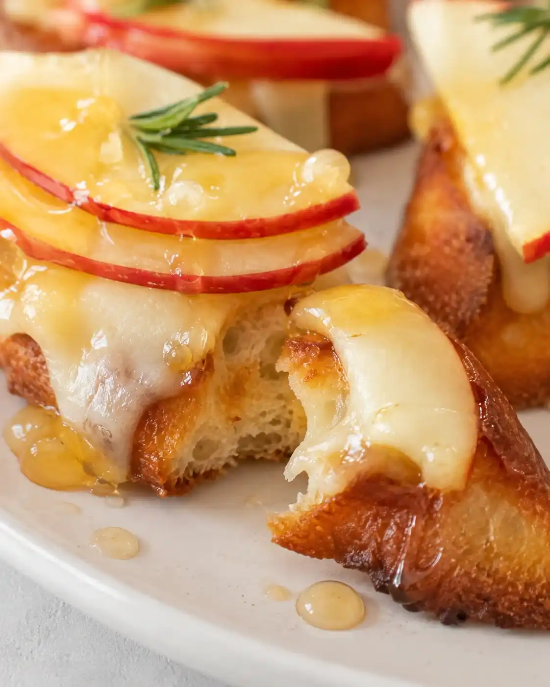 Crostini with a bite taken showing interior crumb, melted cheese and apple slices with honey