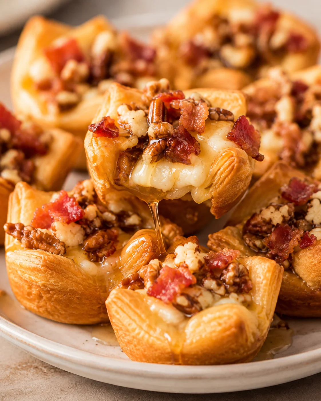 A single Easy Bacon Brie Bite being lifted with melted cheese and maple syrup dripping