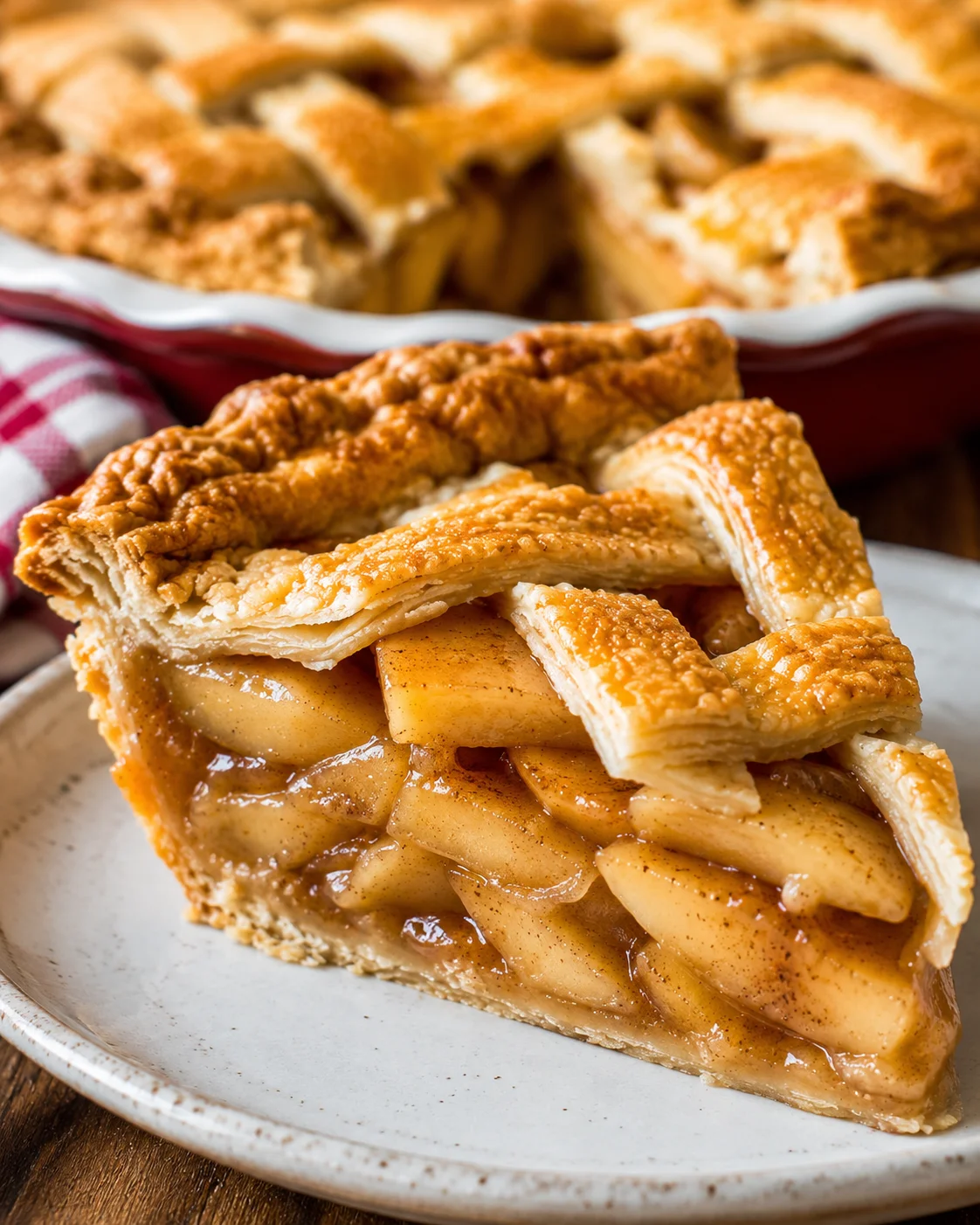 Slice of apple pie on a plate with the pie in the background