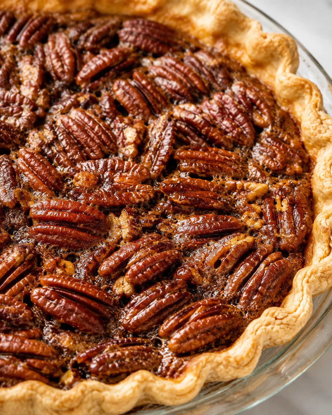 Close-up of a whole pecan pie with glossy toasted pecans and a crimped flaky crust