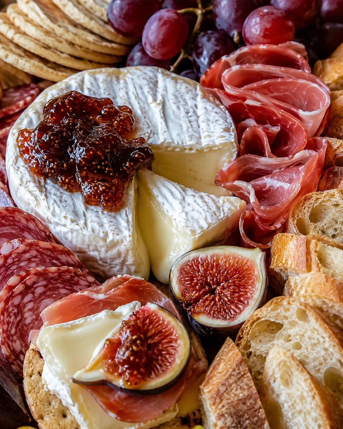 Creamy wheel of brie with a wedge removed and fig jam on top on a Thanksgiving charcuterie board