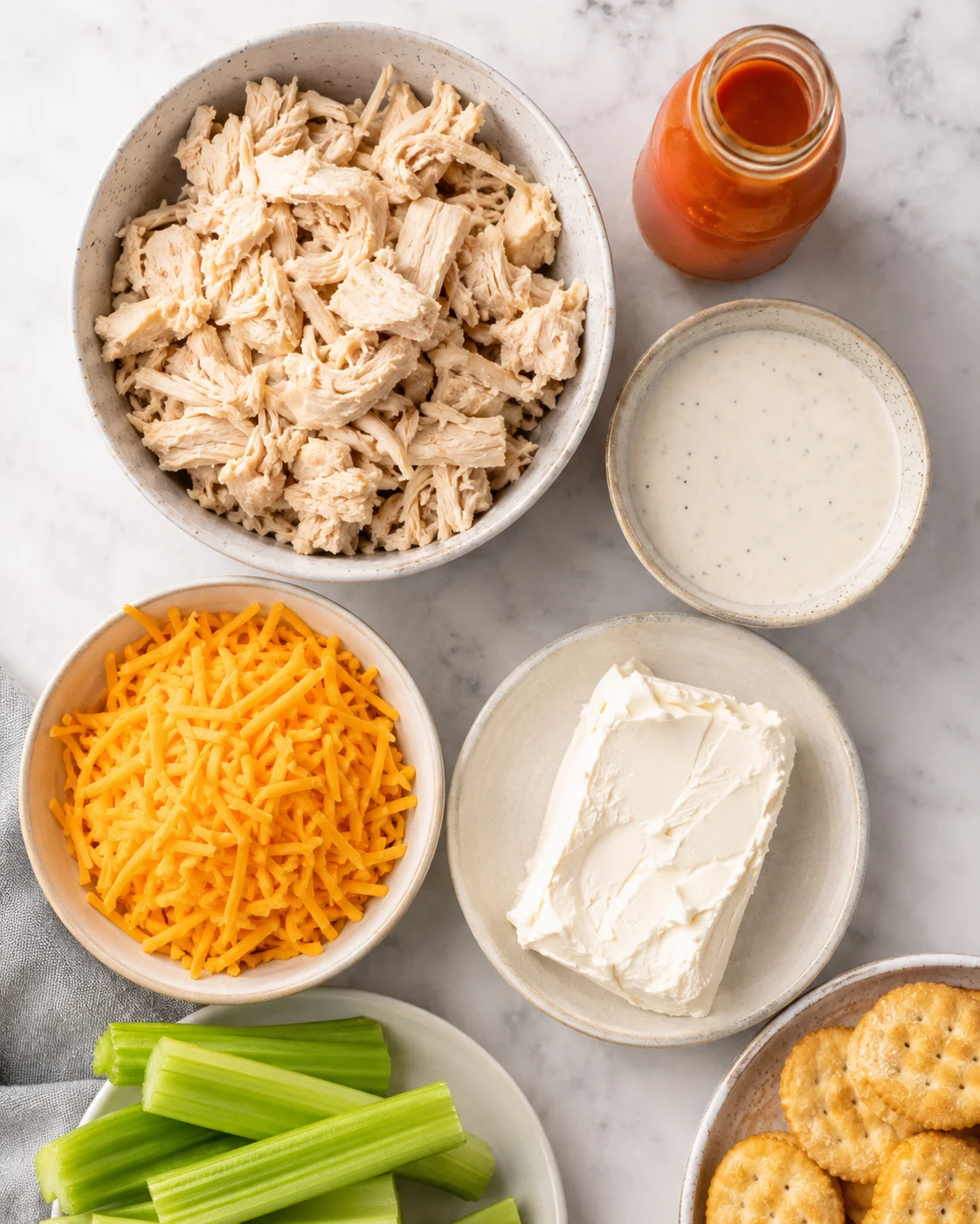 Top-down arrangement of shredded chicken, cheddar, cream cheese, ranch, buffalo sauce, celery and crackers