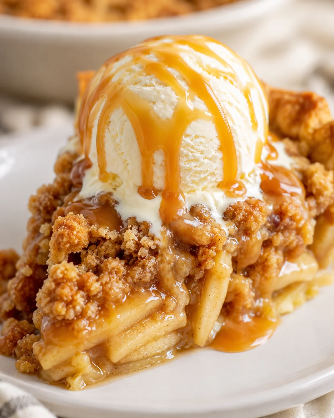 Close-up of a slice of caramel apple pie with a scoop of vanilla ice cream and caramel drizzled on top