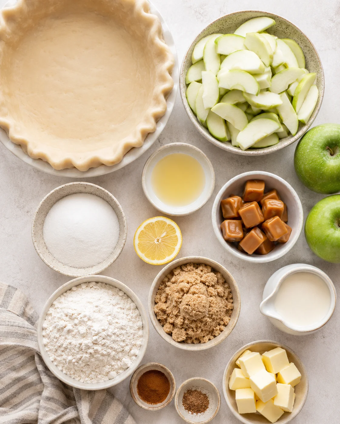 Top-down view of ingredients for caramel apple pie including pie crust, sliced apples, caramels, flour, sugars, butter and spices