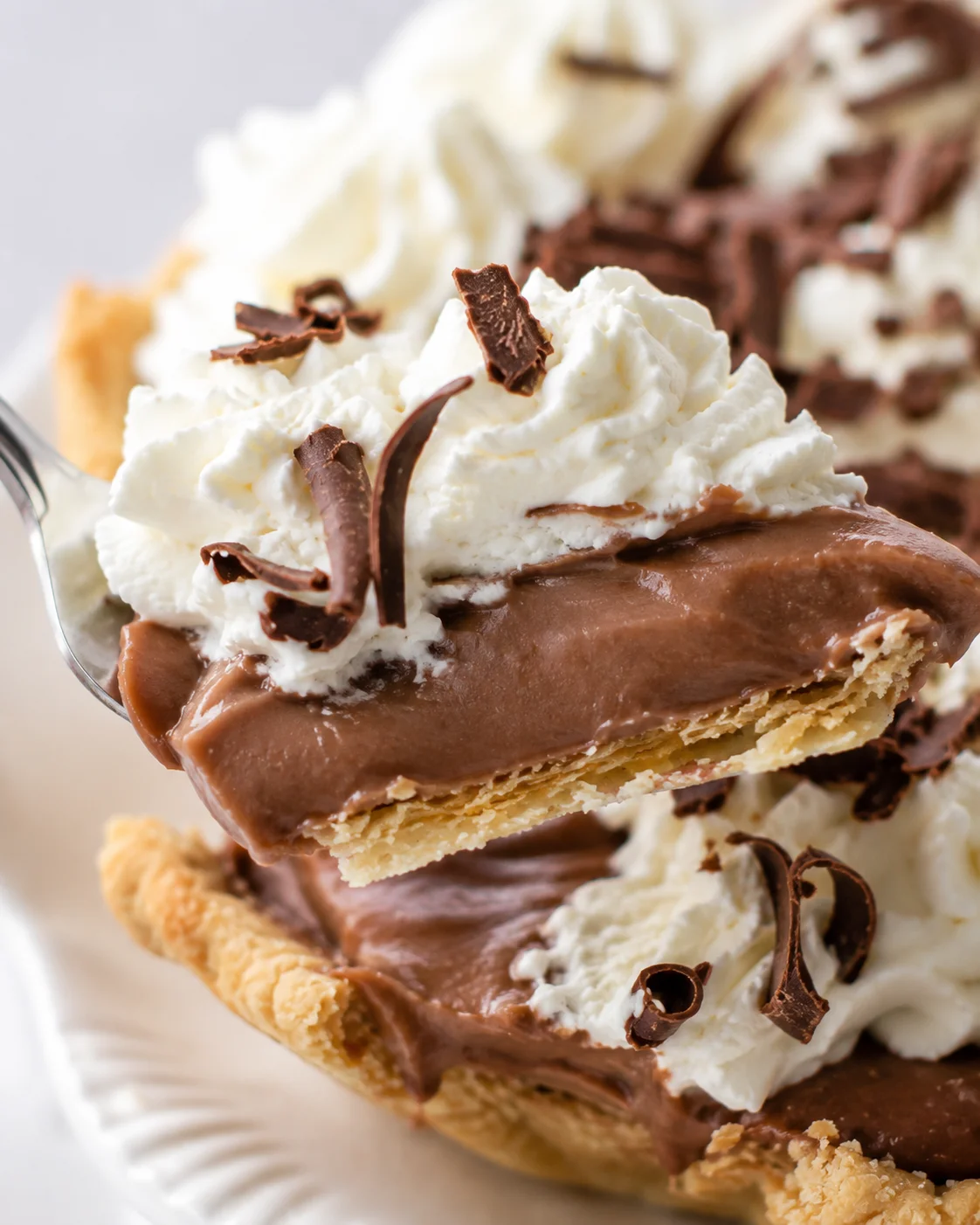 Close-up of a fork lifting a forkful of chocolate cream pie showing creamy filling, crust, whipped cream, and chocolate curls