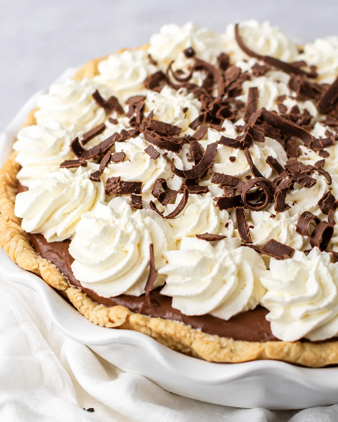 Chocolate cream pie topped with piped whipped cream and chocolate curls in a white pie dish
