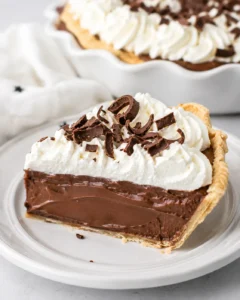 Single slice of chocolate cream pie on a white plate showing creamy chocolate filling, whipped cream, and chocolate shavings