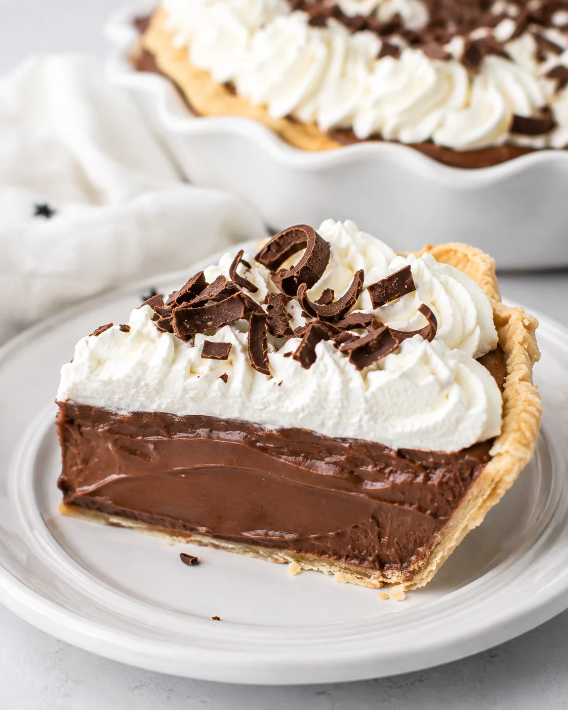 Single slice of chocolate cream pie on a white plate showing creamy chocolate filling, whipped cream, and chocolate shavings