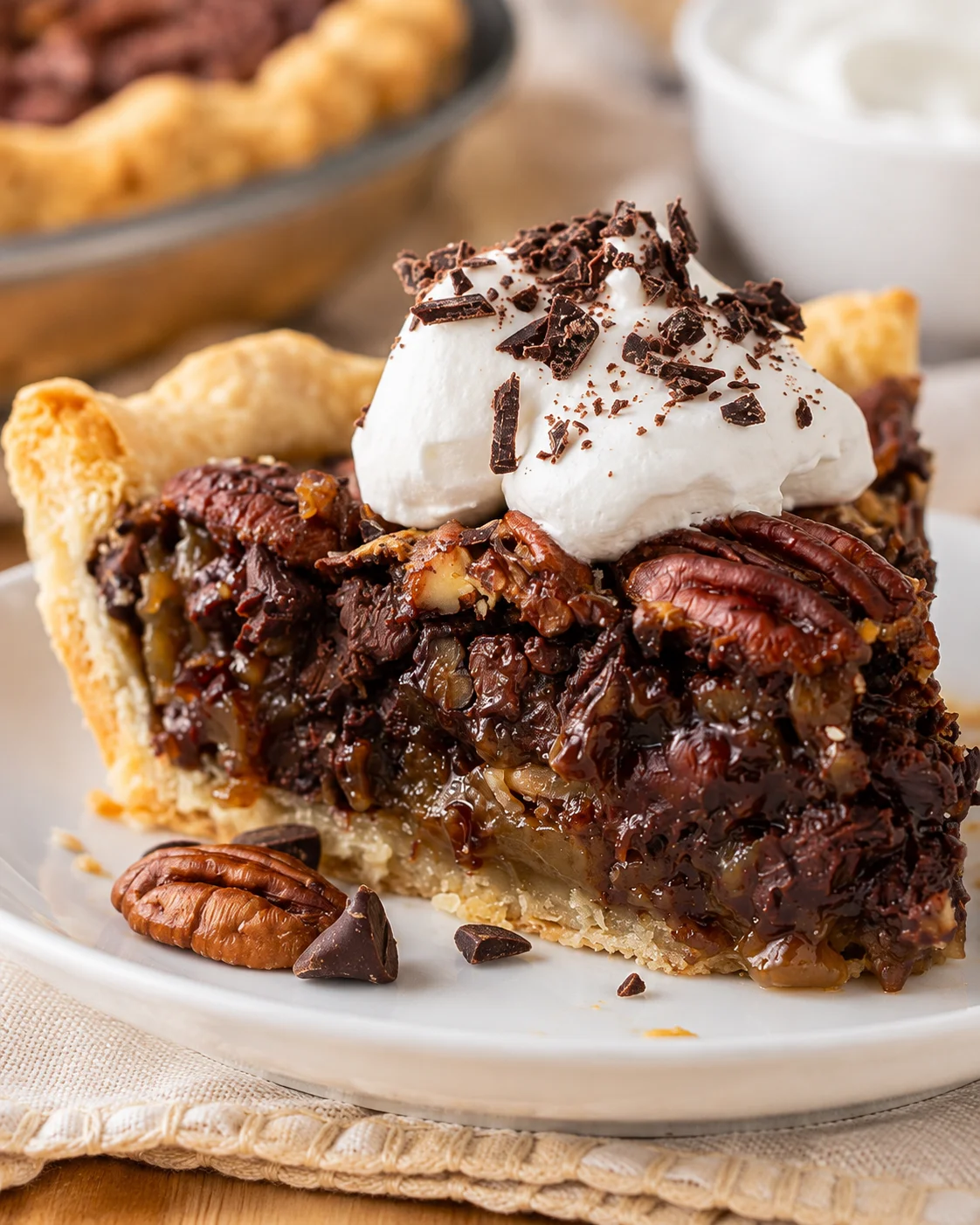 Slice of chocolate pecan pie topped with whipped cream and chocolate shavings
