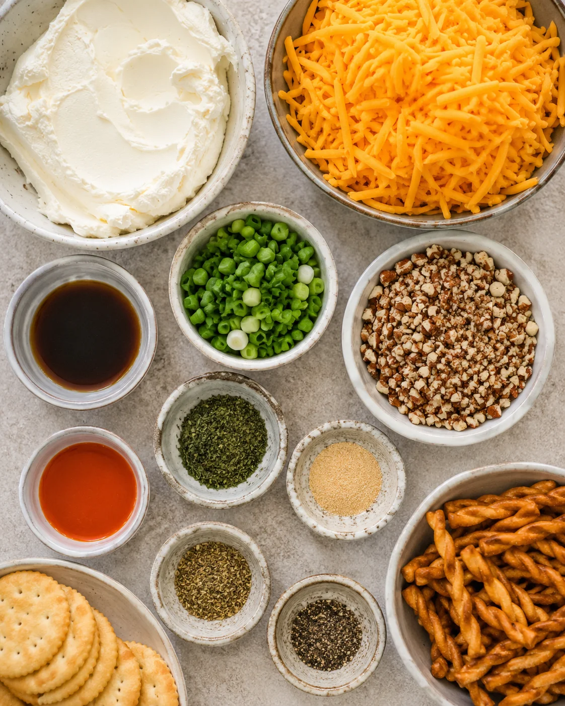 Top-down arrangement of cream cheese, shredded cheddar, green onions, pecans, sauces and spices for a classic cheese ball