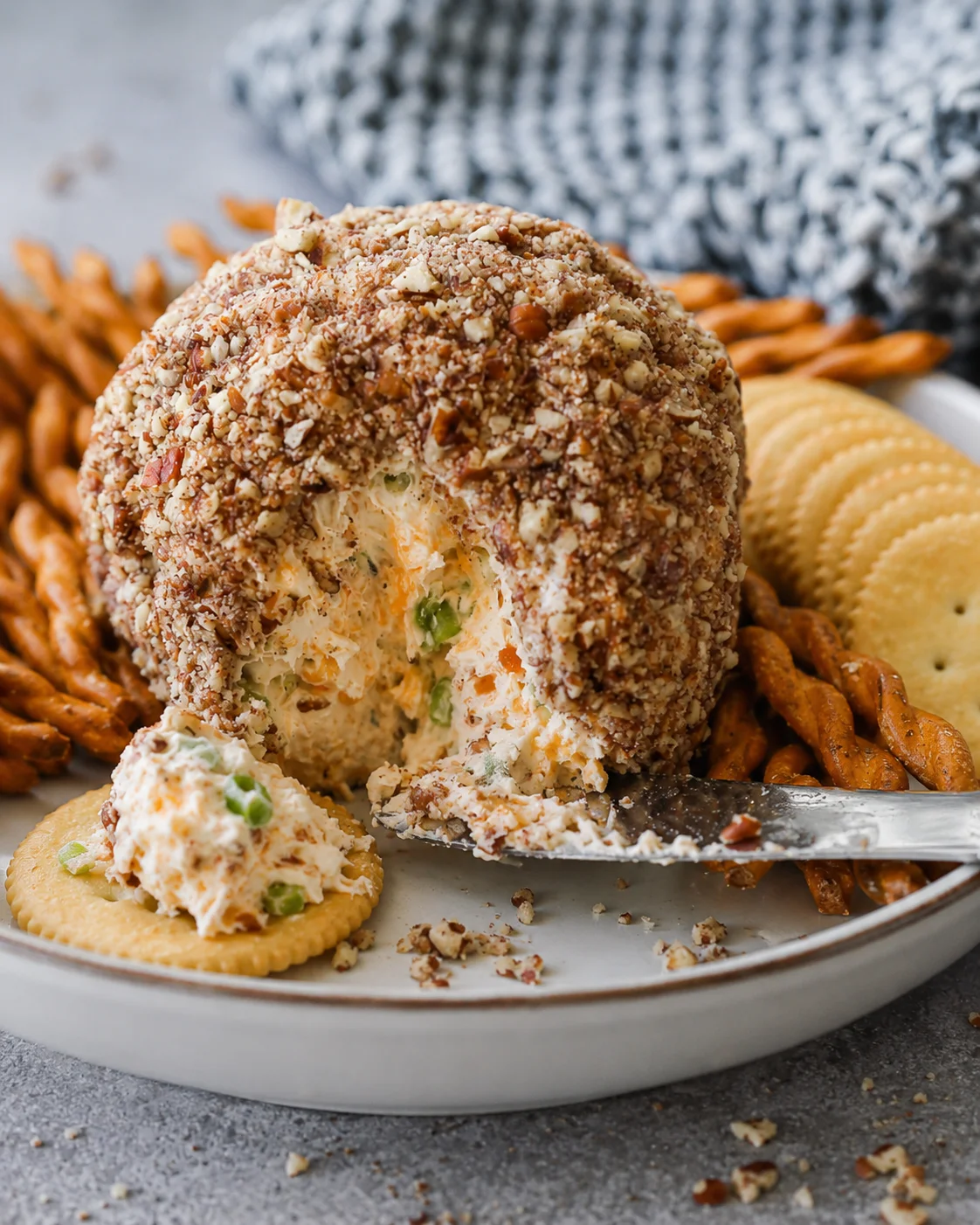 Side view of a classic cheese ball rolled in nuts with a cracker topped with a scoop of cheese