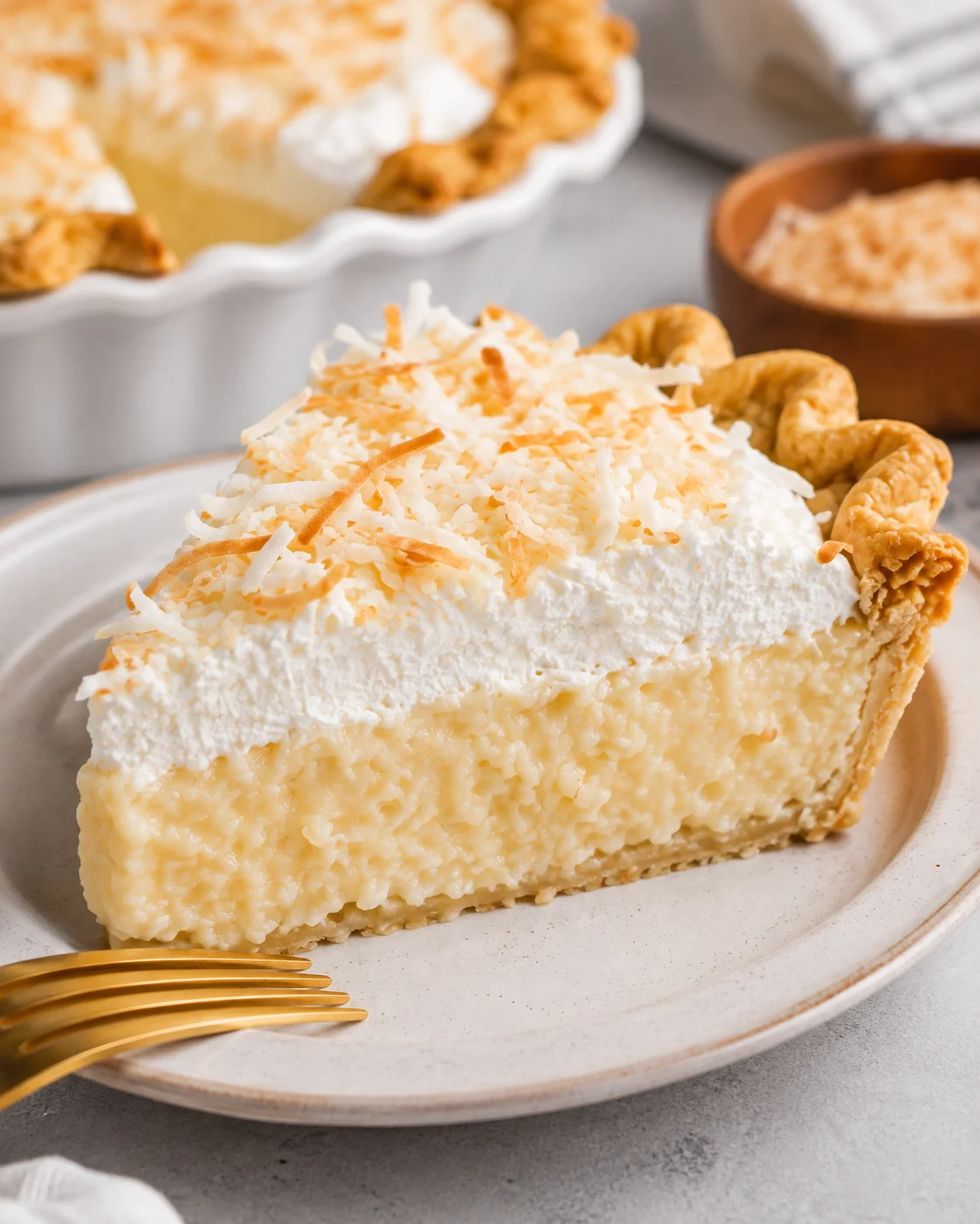 Plated slice of coconut cream pie topped with whipped cream and toasted coconut