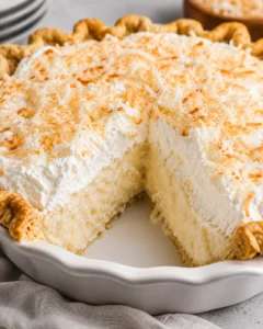 Whole coconut cream pie in a dish with a slice removed, topped with whipped cream and toasted coconut