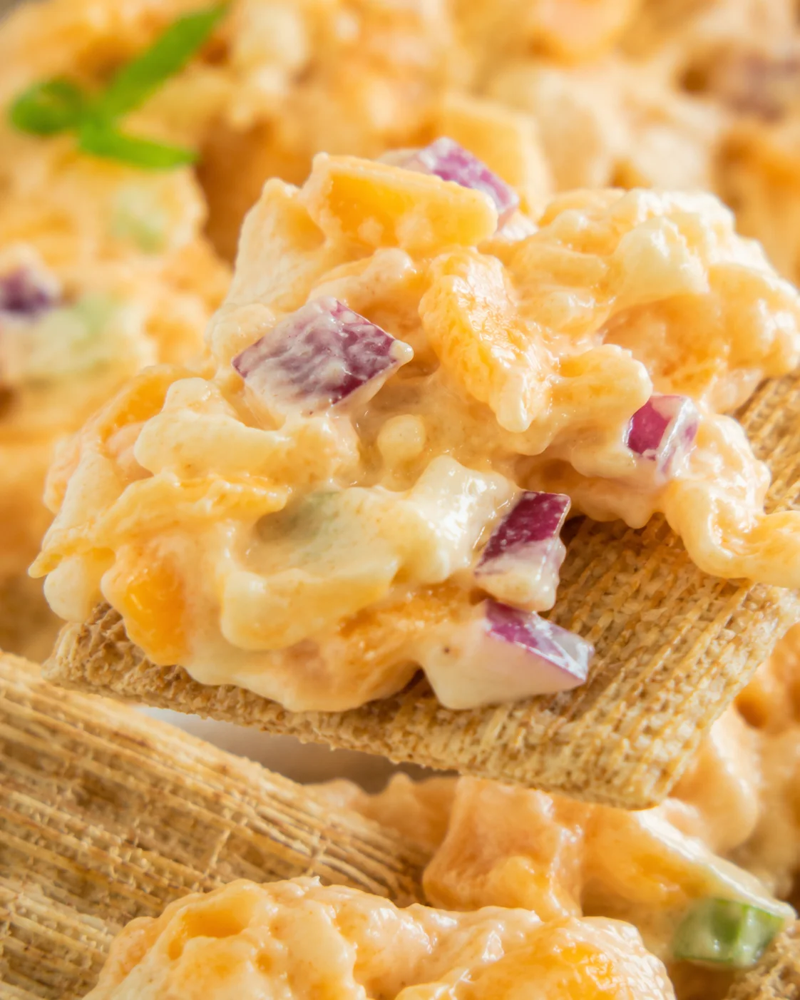 Close-up detail of 5 minute crack dip on a cracker showing shredded cheese and diced red onion